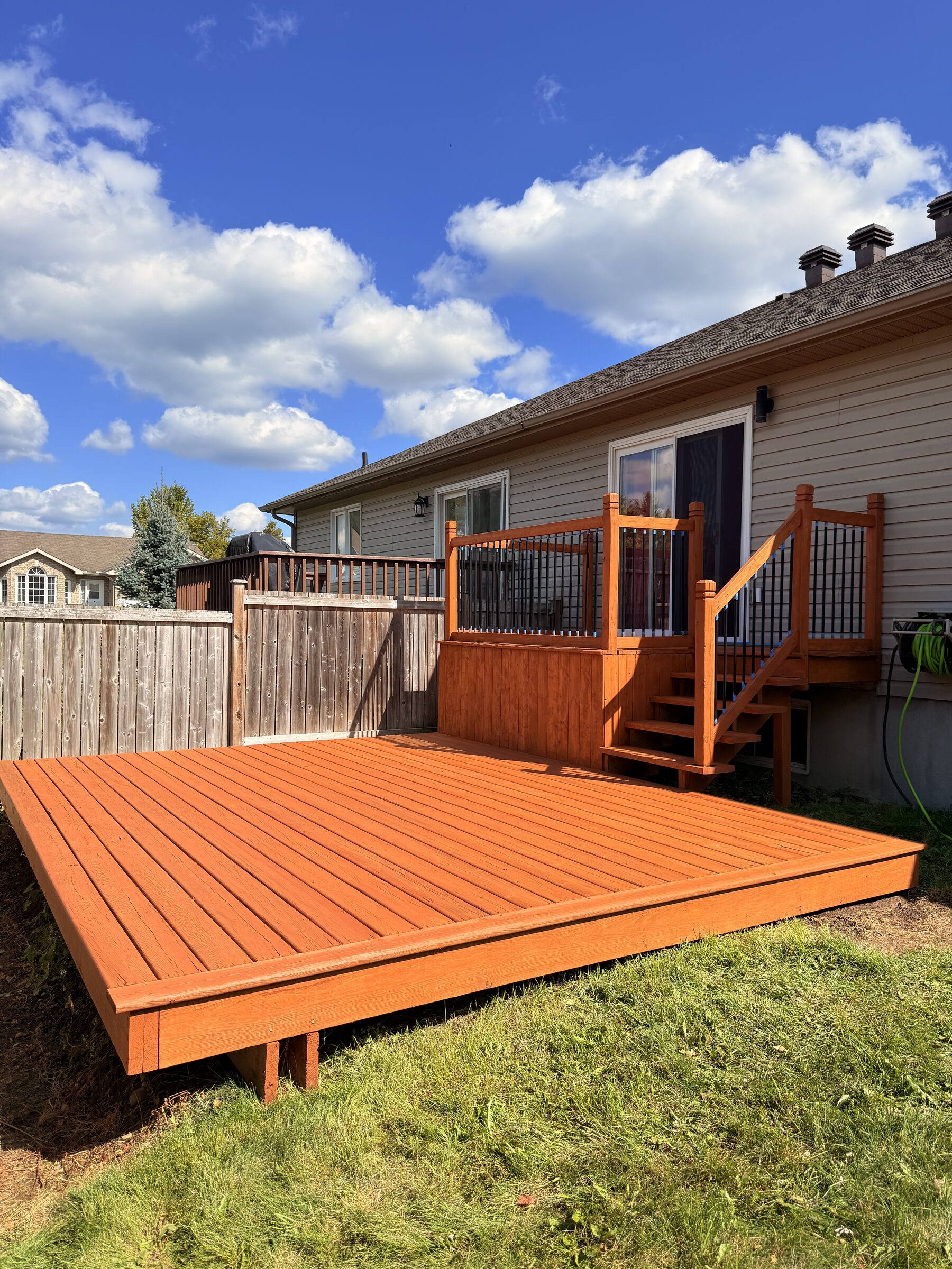 After: Newly stained deck in a rich reddish-brown finish below a red-railed upper deck