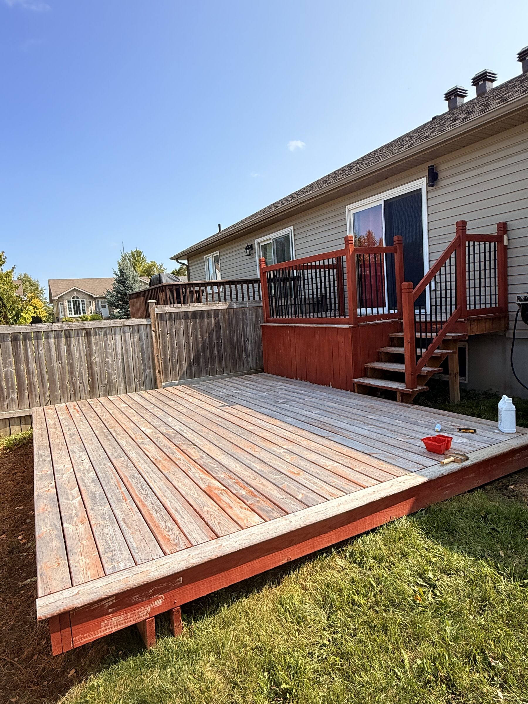 Before: Faded bare wood deck with a stain tray and brush mid-project