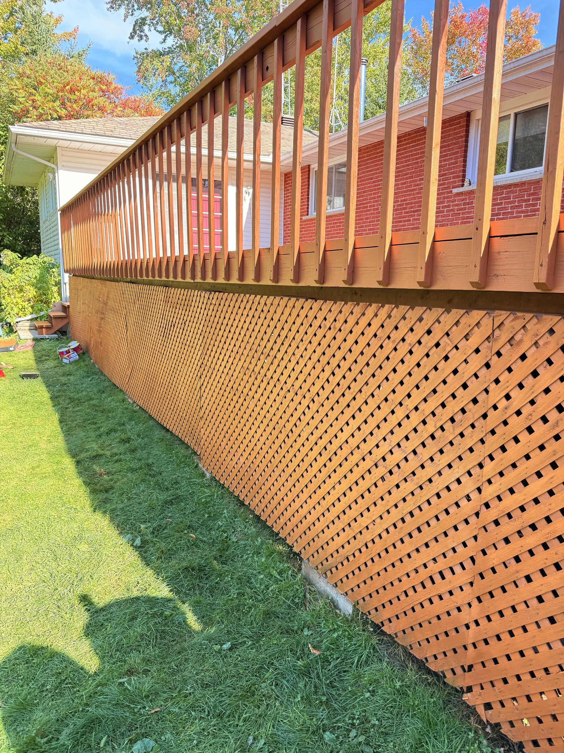 After: Freshly stained deck with matching railing and diamond lattice skirting against the red brick wall