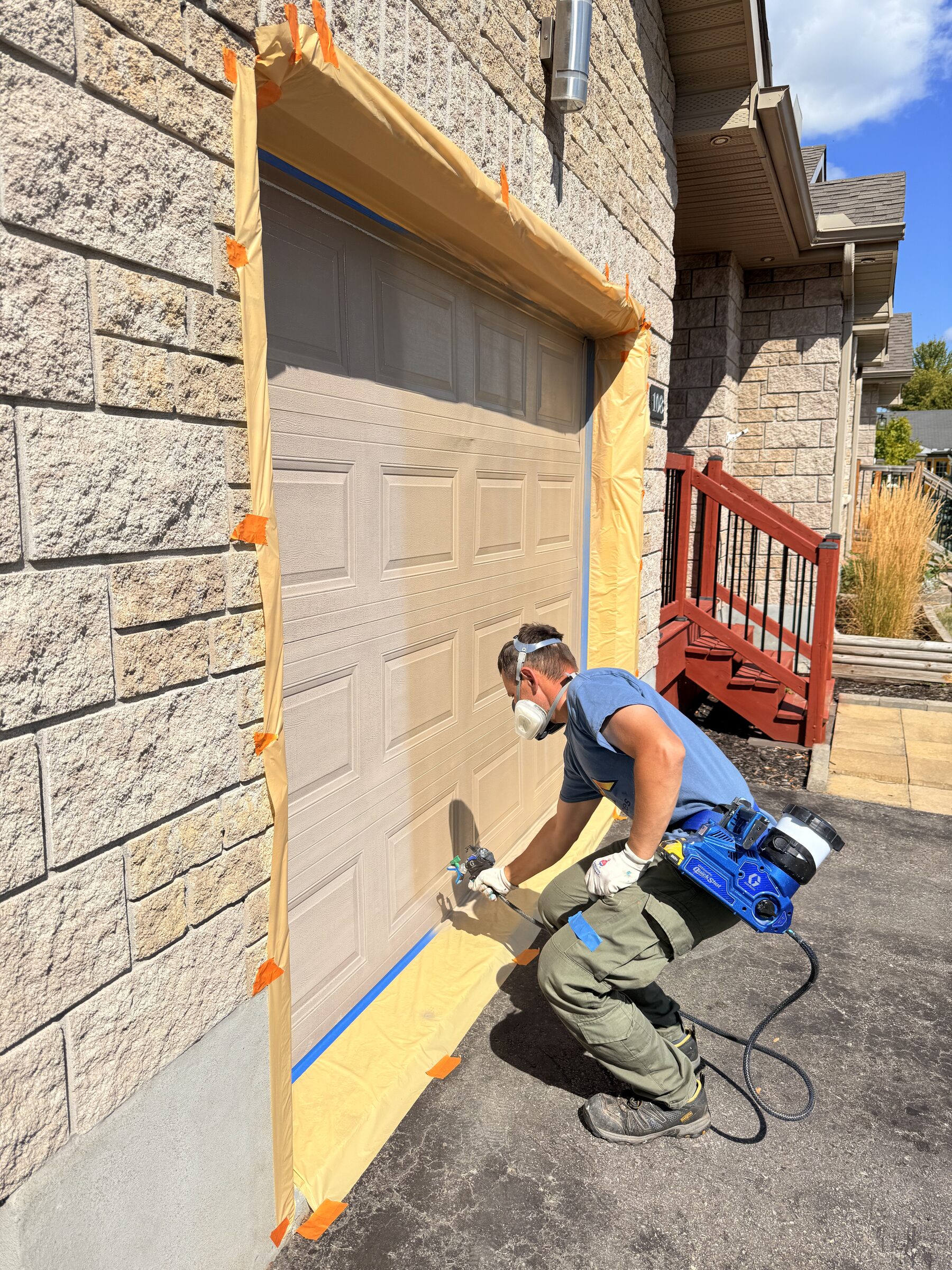 Before: Garage door being spray-painted, surrounding wall masked off