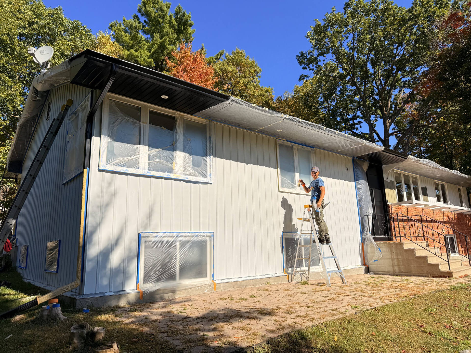 Before: House corner masked with plastic sheeting and tape, concrete steps and black railing