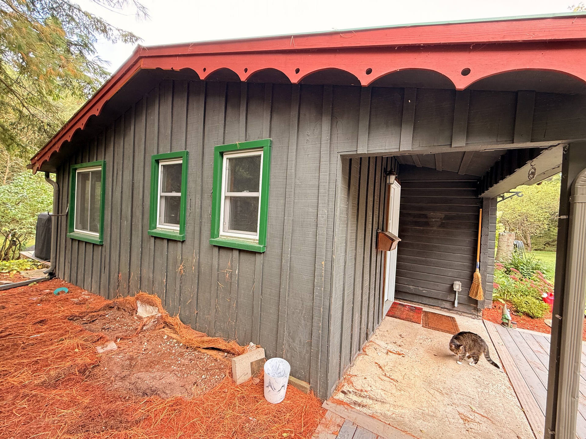 Before: Cottage exterior in dark faded siding with green window trim and scalloped gable trim