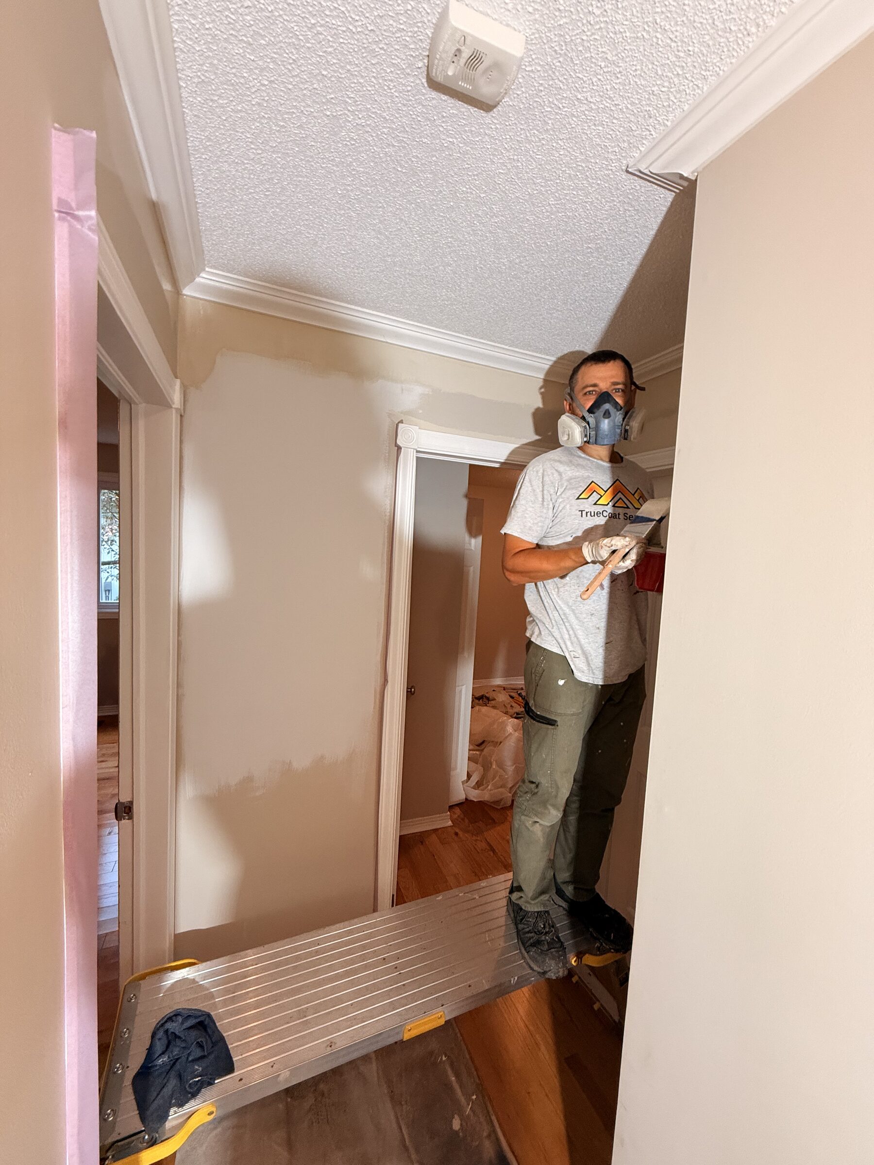 TrueCoat painter in a respirator on a step platform in a hallway with freshly patched walls